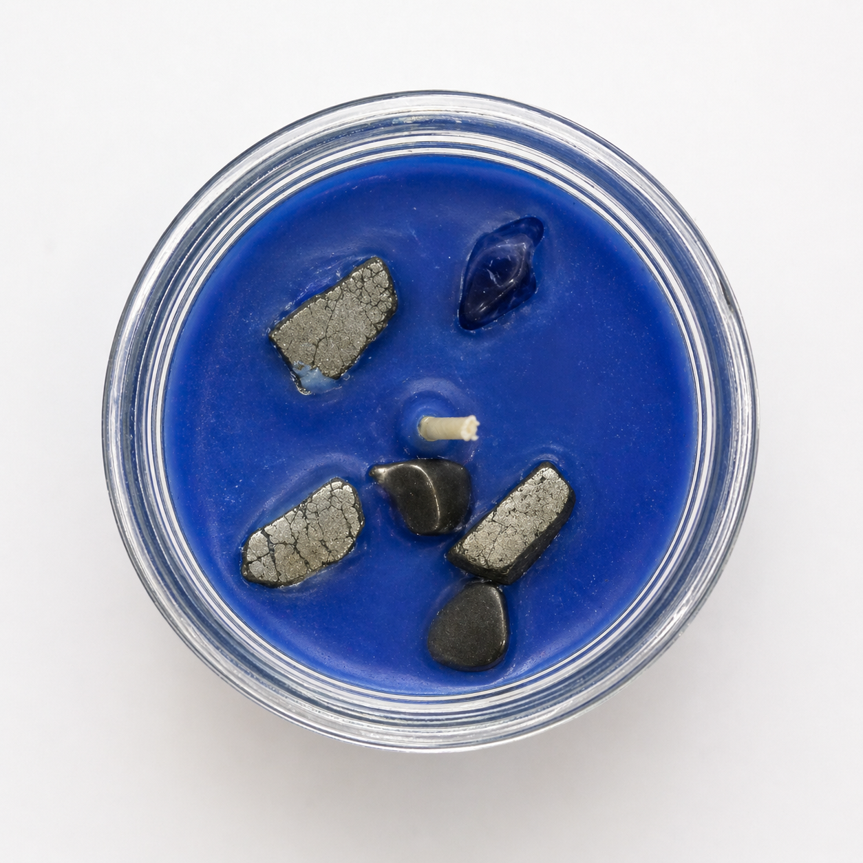 Blue candle in a clear container with decorative stones on a white background