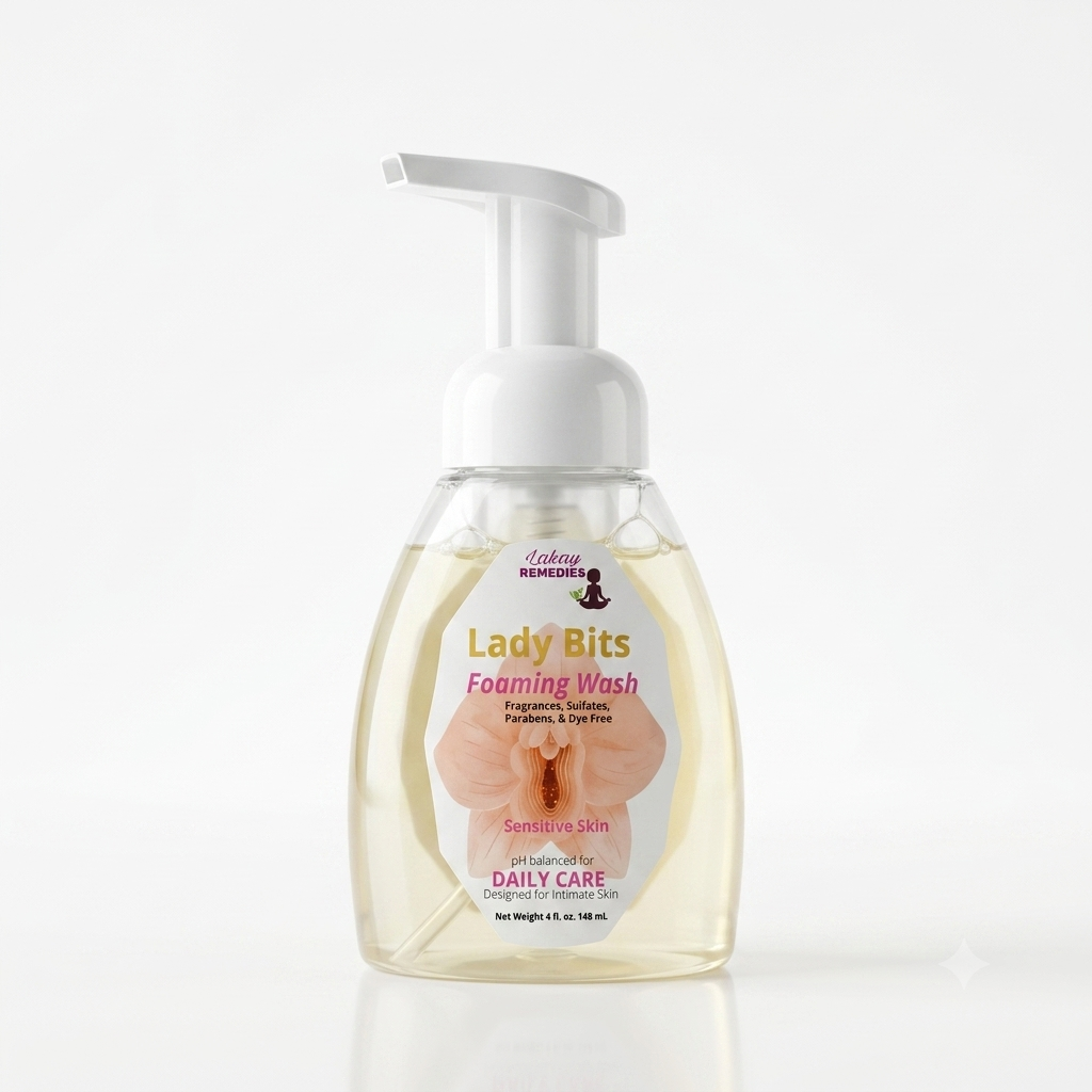 A bottle of Lady Bits Foaming Wash, featuring a clear plastic bottle filled with pale yellow liquid, a white pump dispenser, and a white label with pink and gold text and an orchid graphic.
