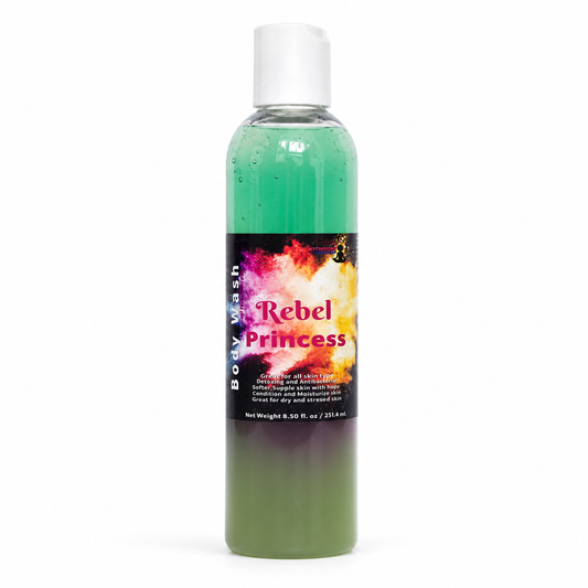 A bottle of Rebel Princess Body Wash featuring a clear plastic bottle with a white cap. The product is shown split horizontally to display its dual-color identity: a bright green top half and a dark olive-green bottom half, separated by a black label with a colorful fiery graphic and pink text.