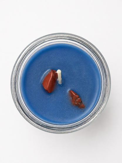 Blue candle in a glass jar with two small figurines on a white background