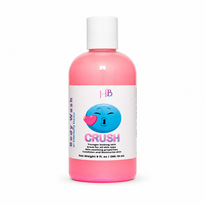 A pink bottle of Her Beauty Factory Body Wash 'CRUSH' with a white cap and a white label featuring a blue emoji graphic, set against a plain white background.