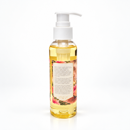 A clear plastic pump bottle filled with golden yellow oil, featuring a white pump dispenser and a floral label on the front, set against a plain white background.
