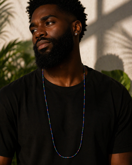 Man wearing a black t-shirt with a colorful necklace, standing against a wall with plant shadows.