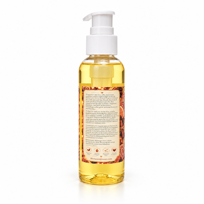 A clear bottle of golden yellow hair oil with a white pump dispenser, showing the back label with text and illustrations, on a white background.