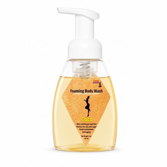A bottle of Coco Foaming Body Wash. The product features a clear bottle filled with golden-yellow liquid, a white pump dispenser, and a textured orange label with a black silhouette of a woman.