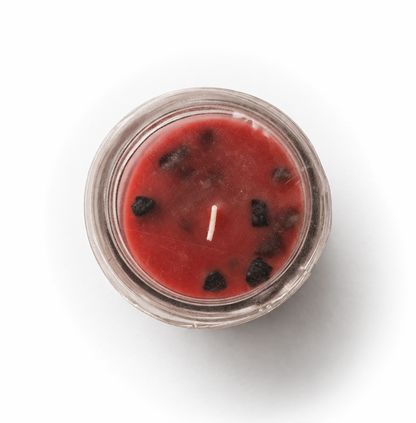 Red candle with dark berries in a glass container on a white background
