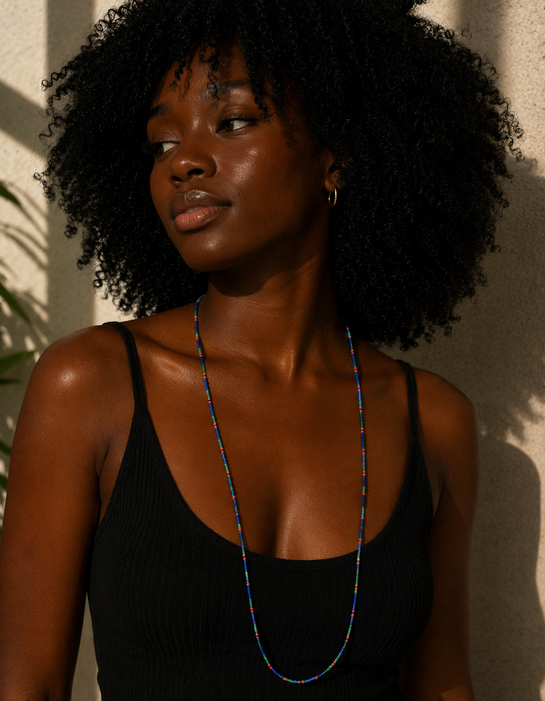 Woman wearing a black tank top and a long necklace against a neutral background