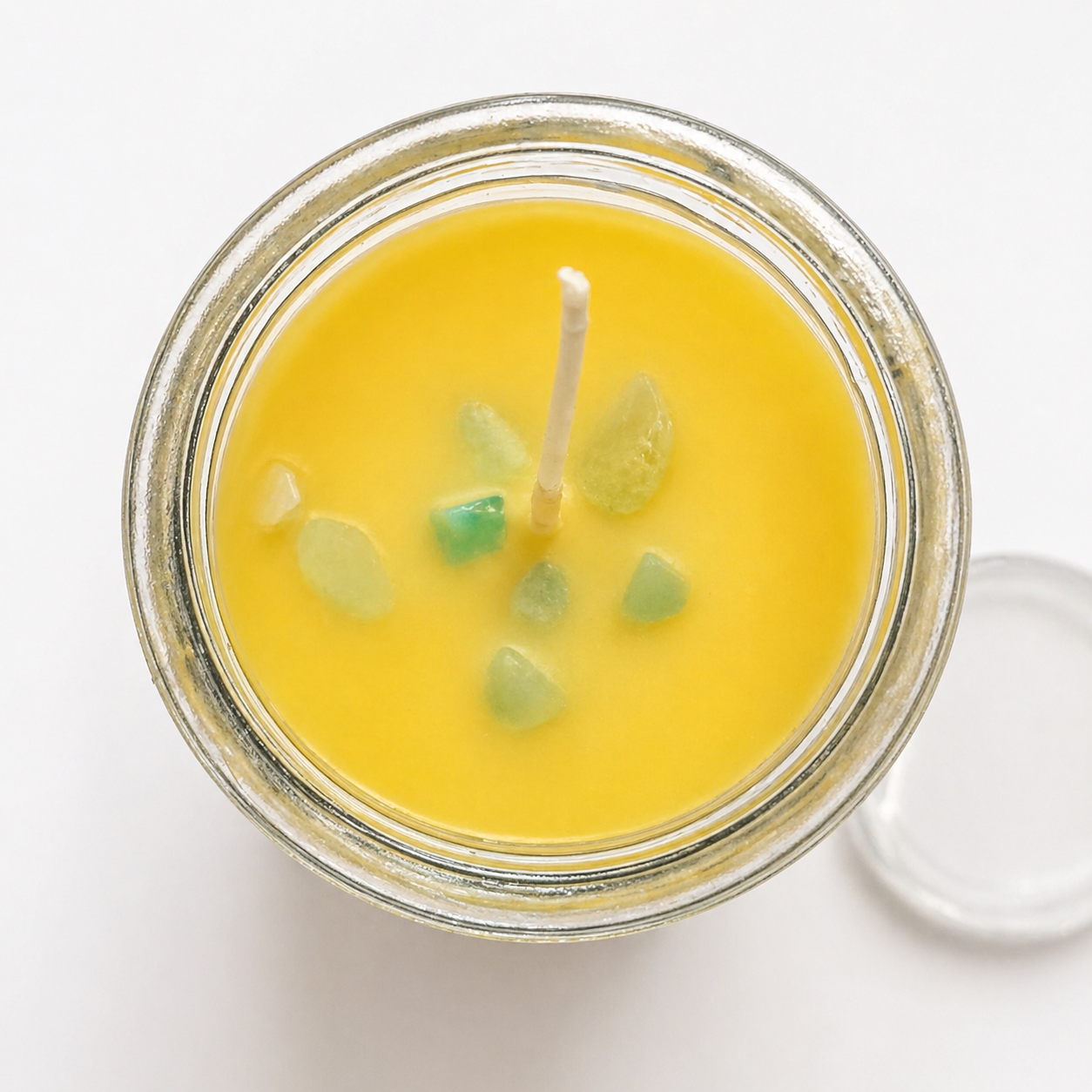 Yellow candle in a glass jar with a wick on a white background