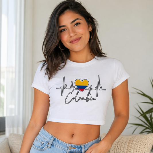 Woman wearing a white t-shirt with a heart and flag design, sitting in a room with a plant in the background.
